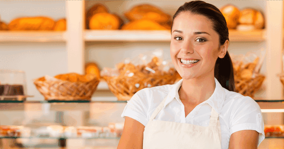 Beautiful young woman in apron keeping arms crossed while standing in bakery shop