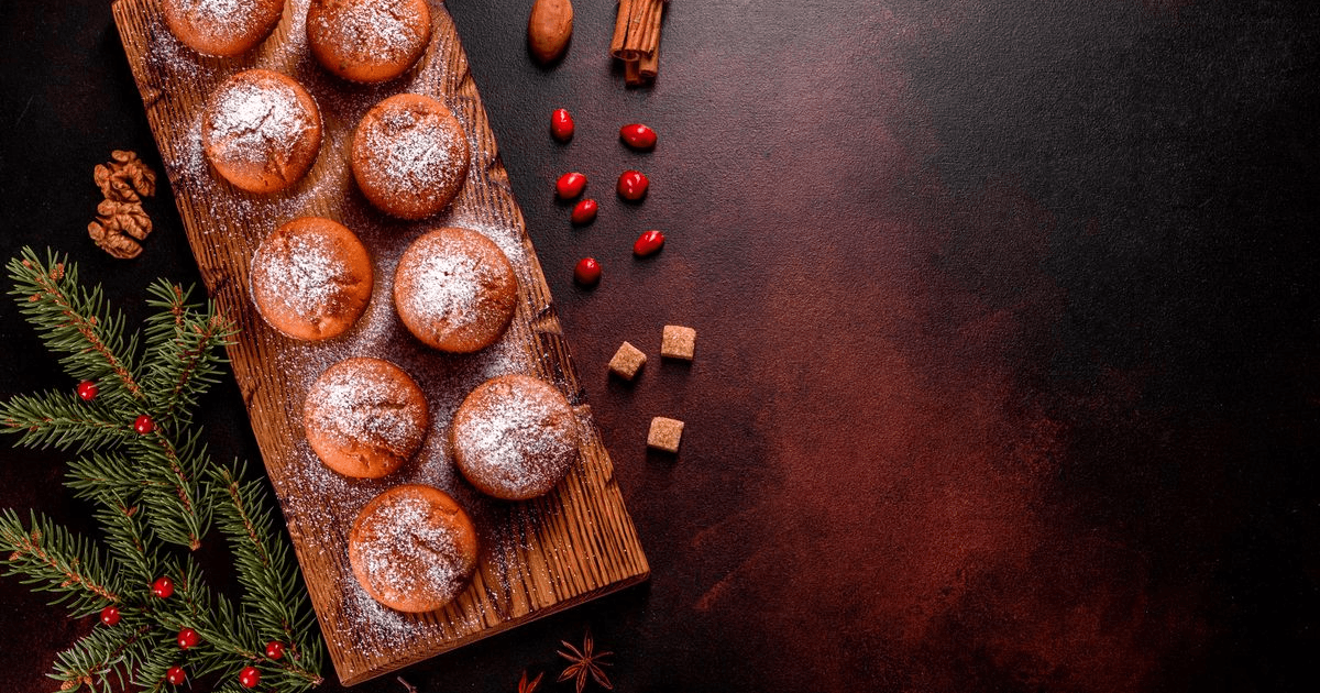 Cocoa muffins dusted with icing sugar on a wooden board with cinnamon sticks and cranberries