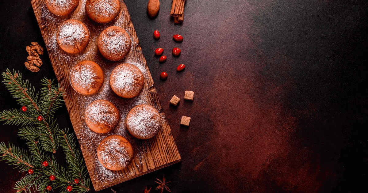 Cocoa muffins dusted with icing sugar on a wooden board with cinnamon sticks and cranberries