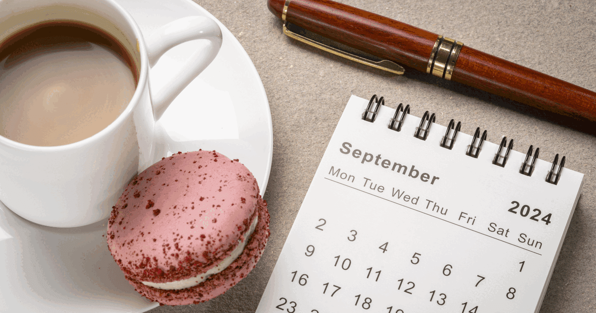 Spiral desktop calendar with a coffee, a macaron and a pen on a stone surface