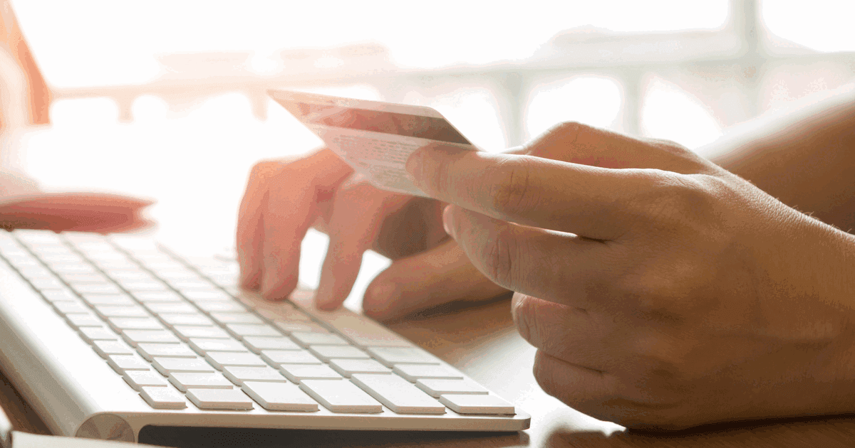 Hands holding a credit card while typing on a keyboard to pay for an order online