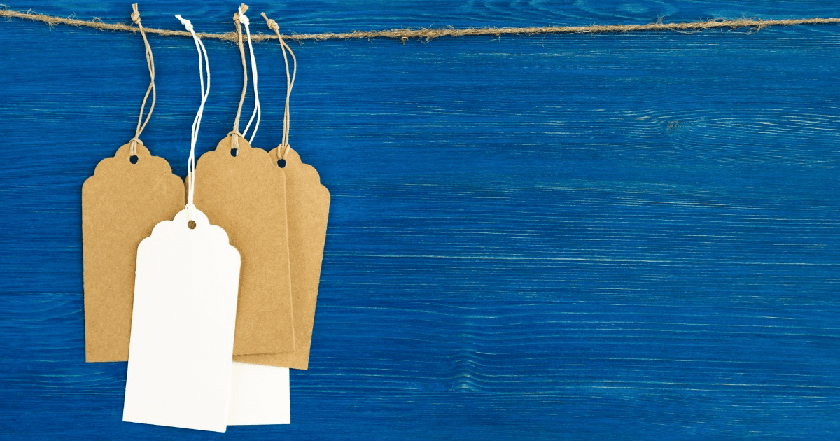 Brown and white blank paper price tags hanging from string against a blue wooden background