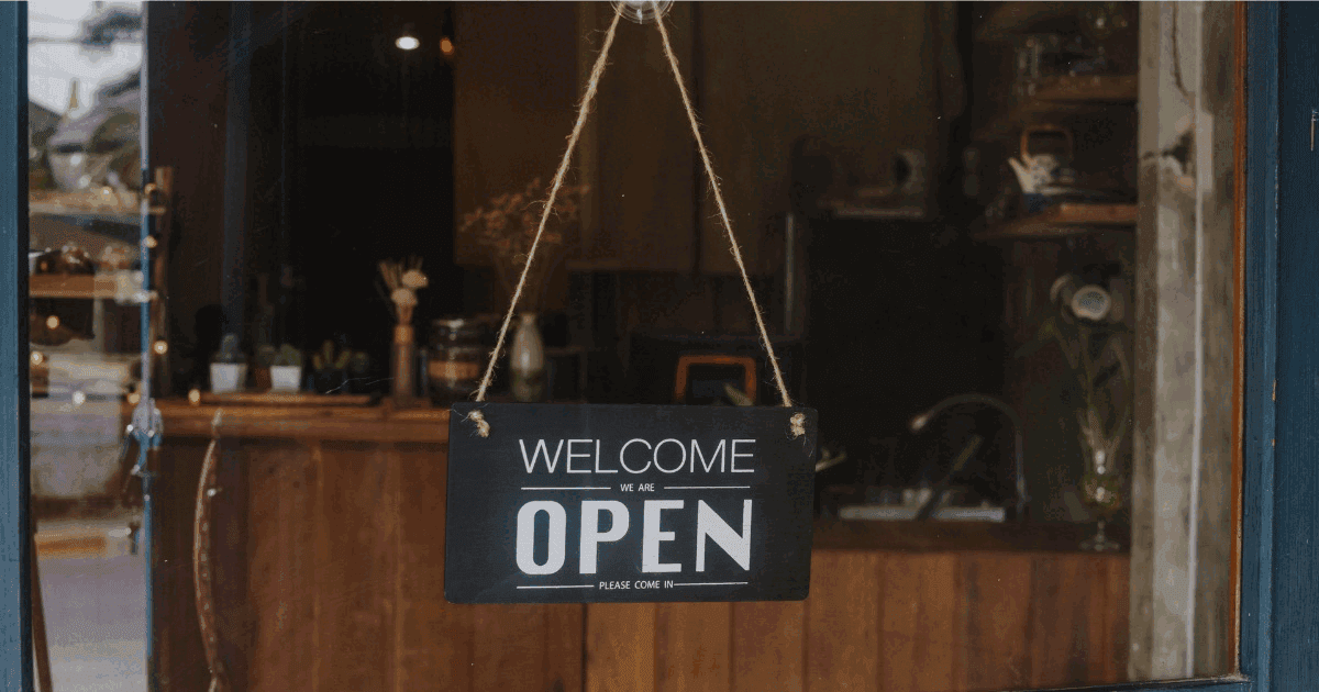 Black retro 'Welcome We're Open' sign hanging in a shop window