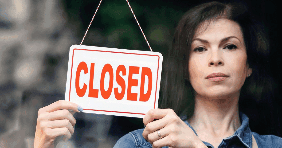 Woman holding a red and white CLOSED sign in a shop doorway