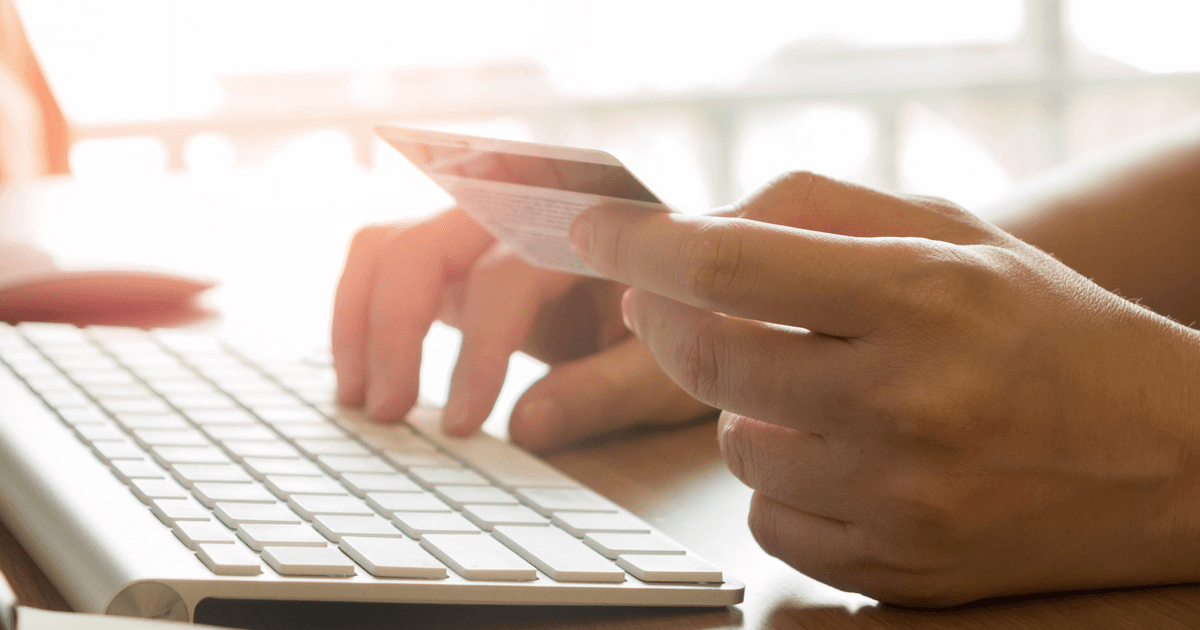 Hands holding a credit card while typing on a keyboard to pay for an order online