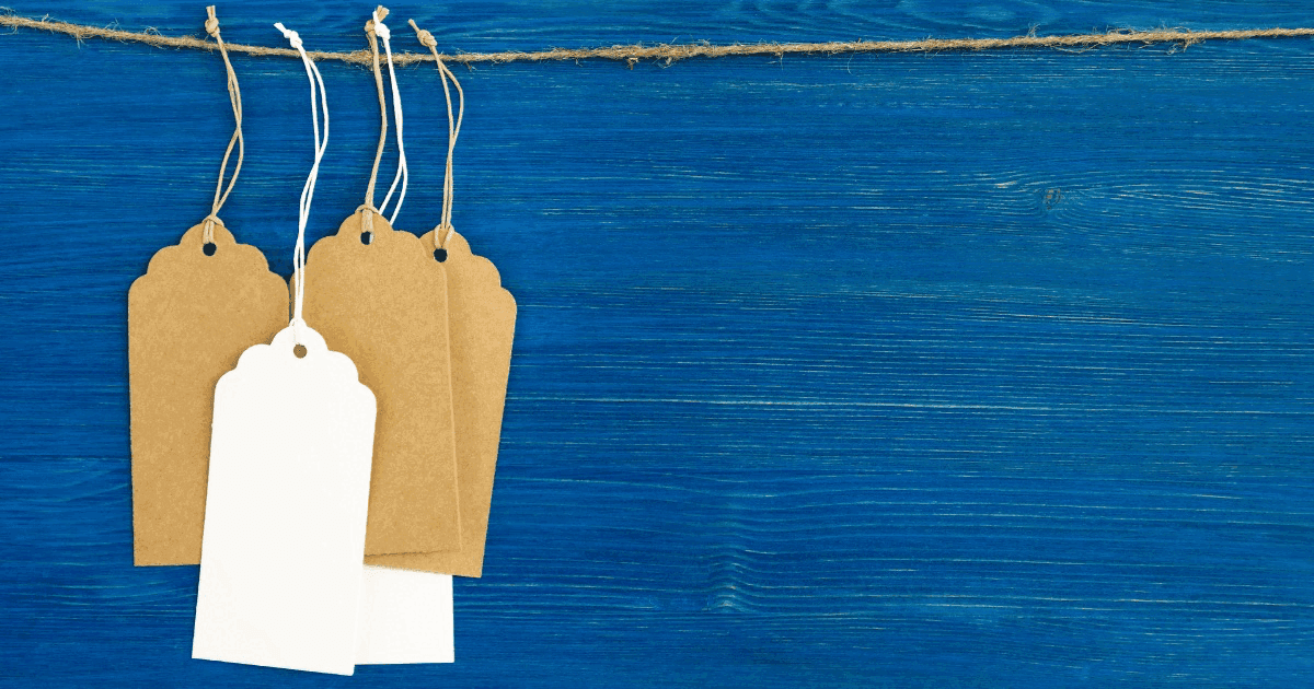 Brown and white blank paper price tags hanging from string against a blue wooden background