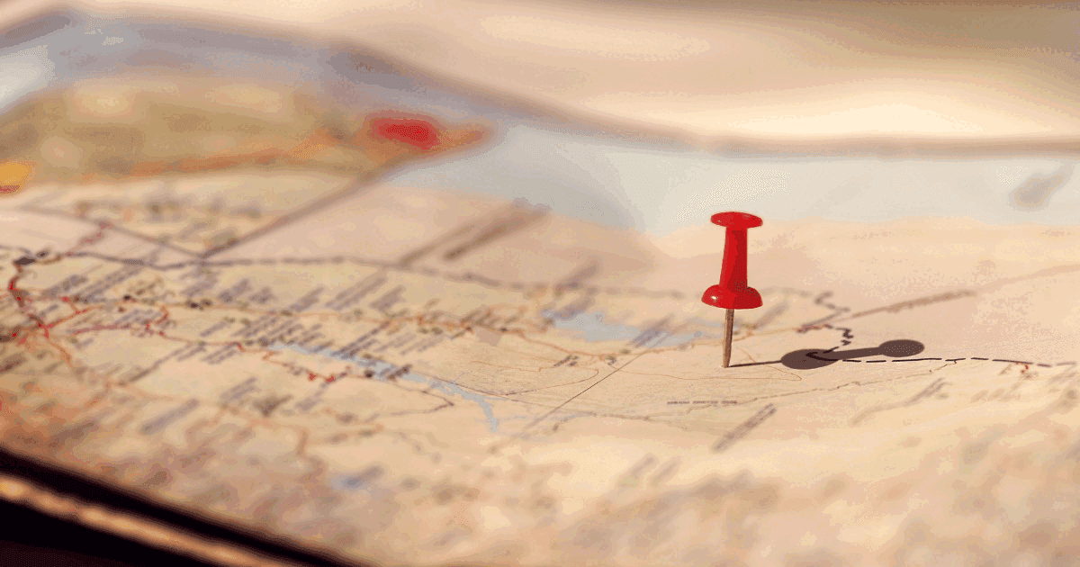 Red pushpin stuck into a paper road map